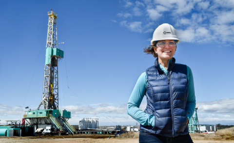 A female engineers stands in front of an oil and gas facility in Denver.