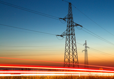 Transmission lines along the side of the road at dusk. Cars zip by leaving only the after shine of their headlights.