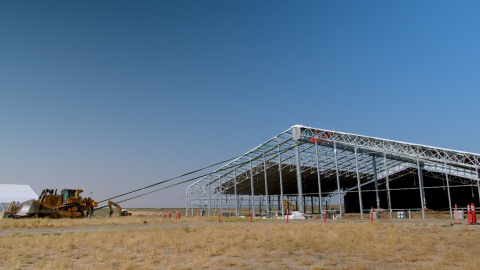 A photo a building only made out of beams, it its attached on ropes to a demolition vehicle
