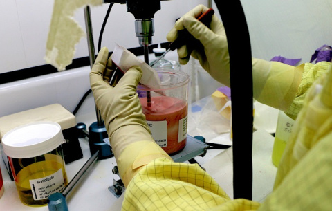 An upclose shot of a scientist wearing gloves and protective gear while preparing a red slurry in a beaker