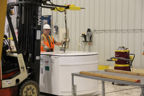 A man in protective gear works on a small white tank with a black machine on it