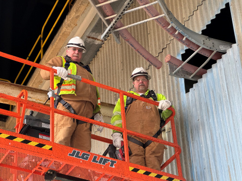 Two employees stand on a raised platform and perform electrical work