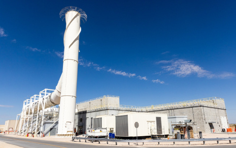 A large white facility building with a tall ventilation pipe coming out of it