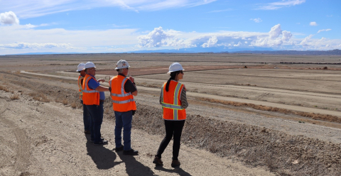 People in orange safety vests and hard hats stand in a large open area