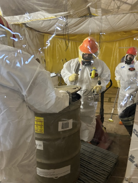 Employees in hazmat suits removing waste from container drums