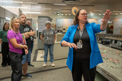 A woman speaking to a small group of people pointing at something behind the camera