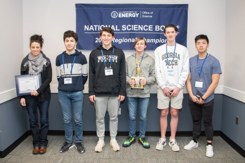 A group of students smile for a photo, one holds a trophy, after winning a science bowl
