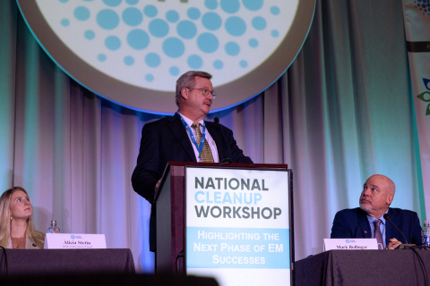 Man in suit speaking behind a podium with a sign that reads, "National Cleanup Workshop."