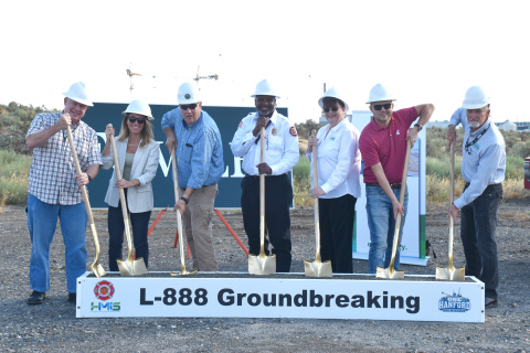 A group of employees in white hats hold shovels while posing for a group photo