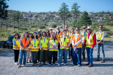 A large group photo of a tour group wearing yellow and orange protective vests