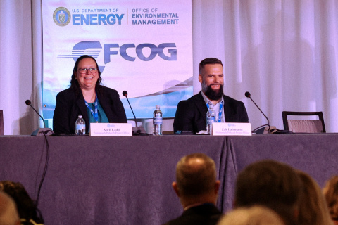 Two individuals sitting at a table speaking at a panel for a conference