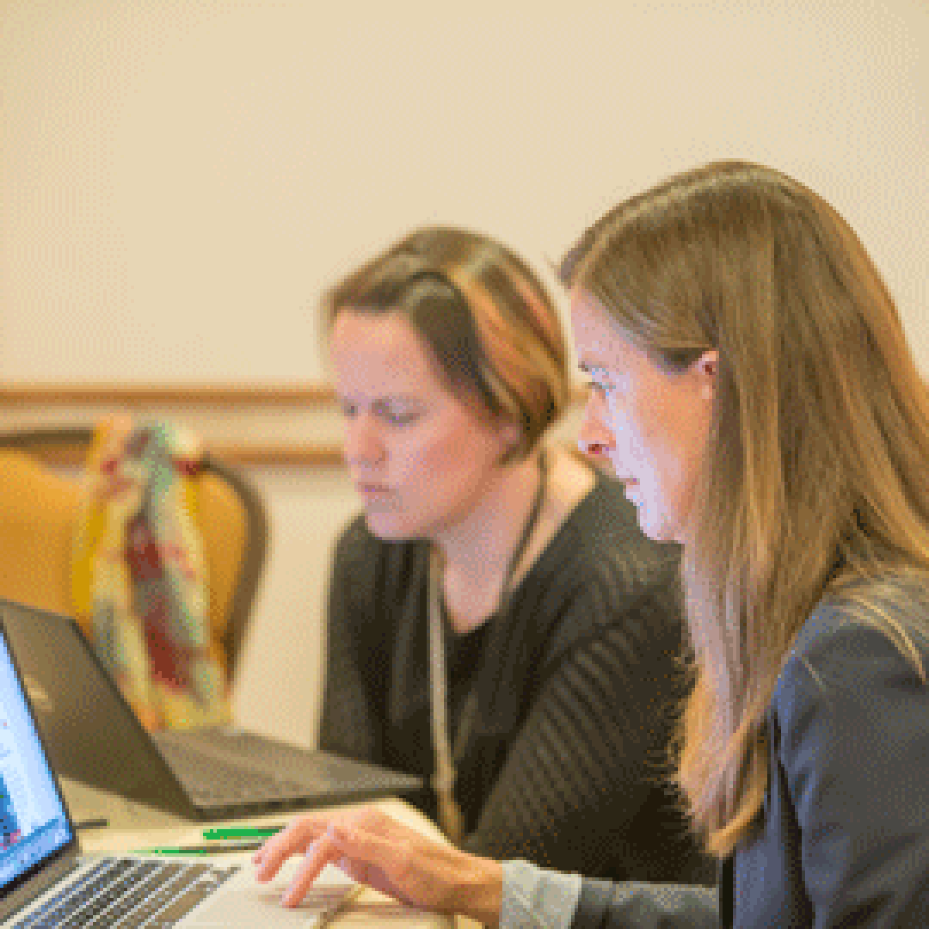 Image shows two women at a table each looking at their own laptop computers.