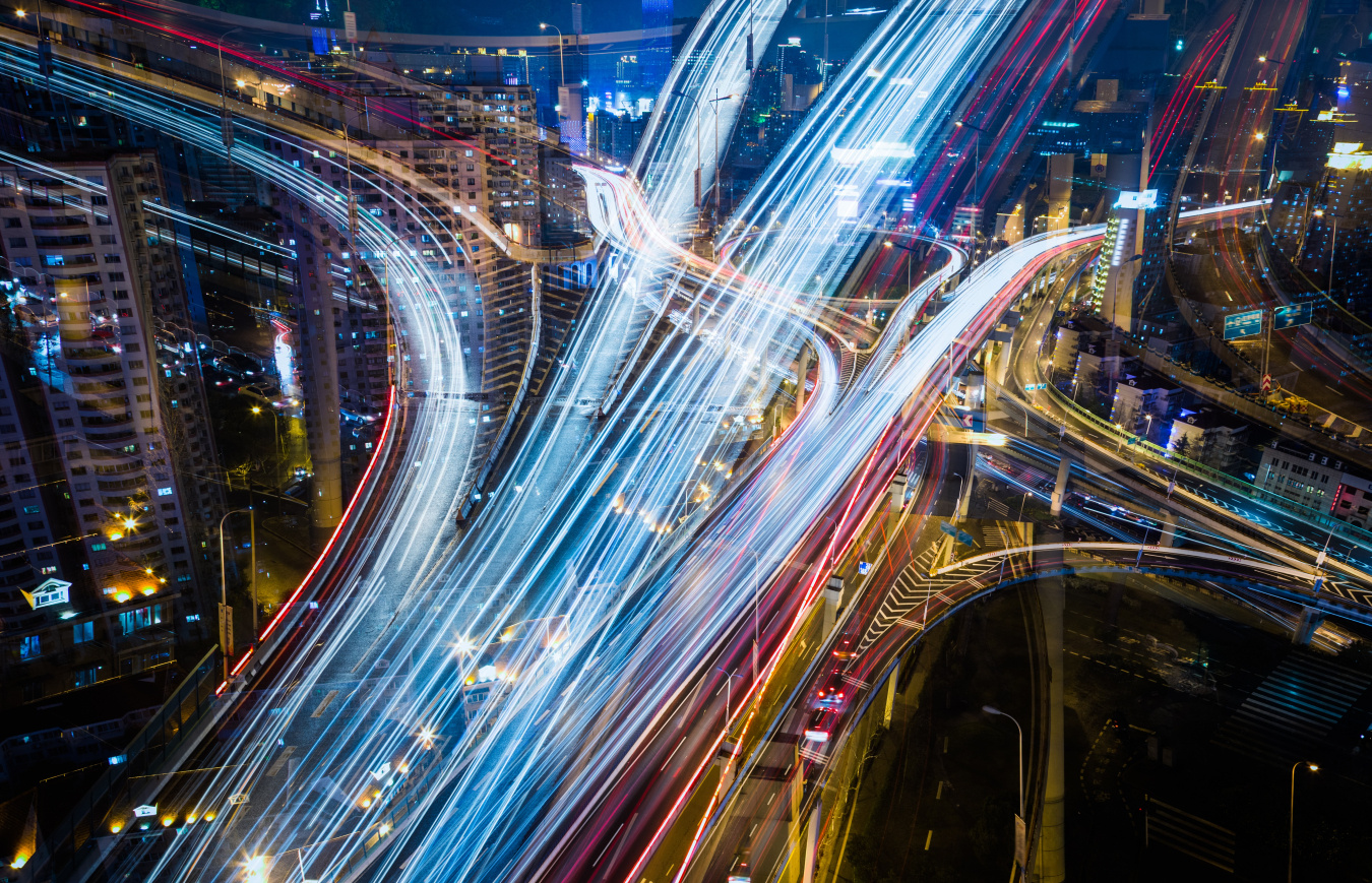 Blurred head and tail lights of cars speeding on highway interchange at night.