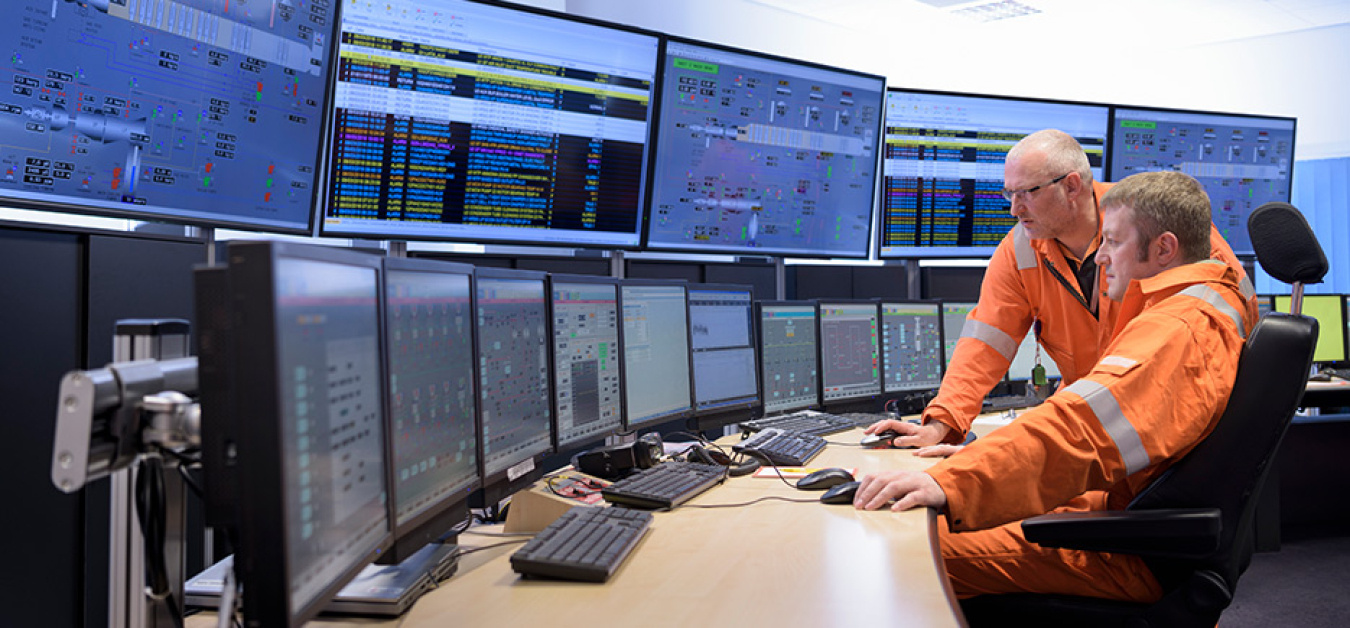 Engineers in a control center viewing many screens.