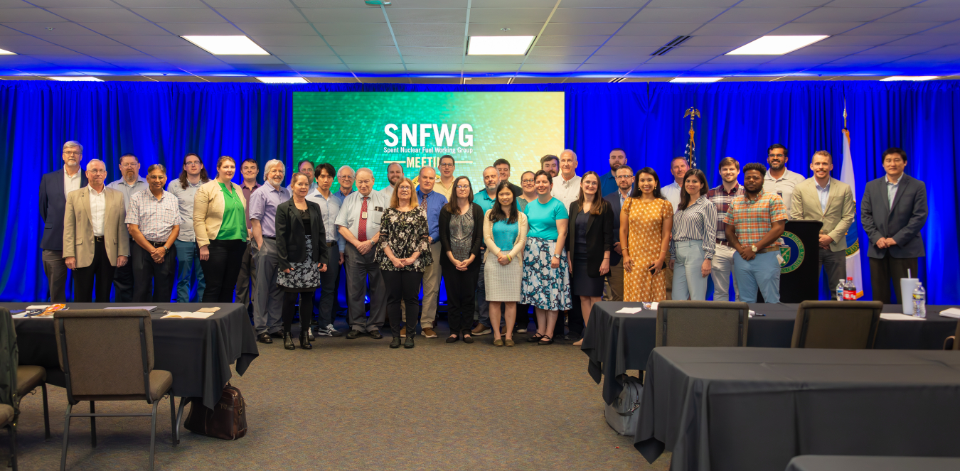 A large group photo of individuals at the front of a room with a bright blue curtained wall behind them