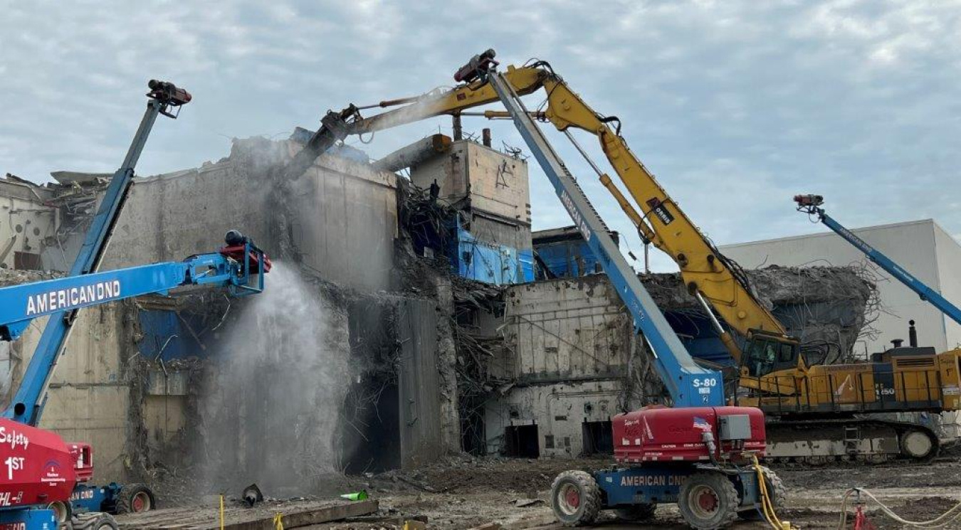 Large construction vehicles work to demolish a building