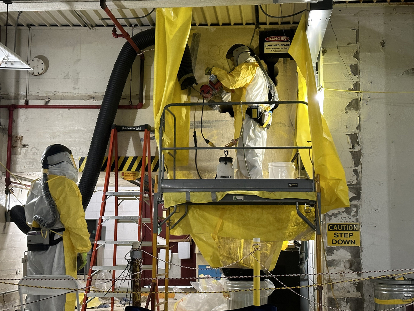 Employees in hazmat gear inside a building that is being demolished