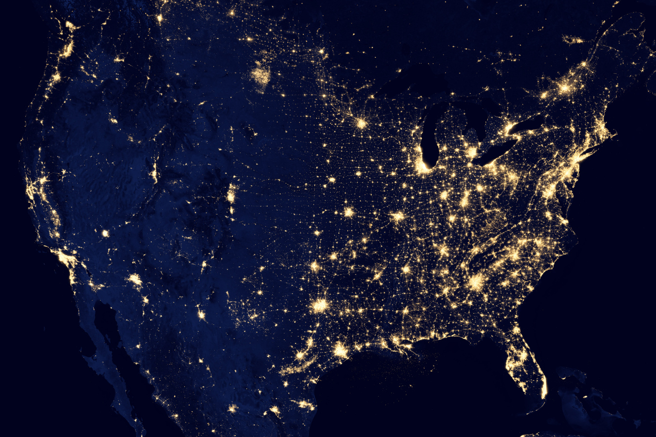 A satellite view of the United States with major cities glowing bright like stars in the night sky.