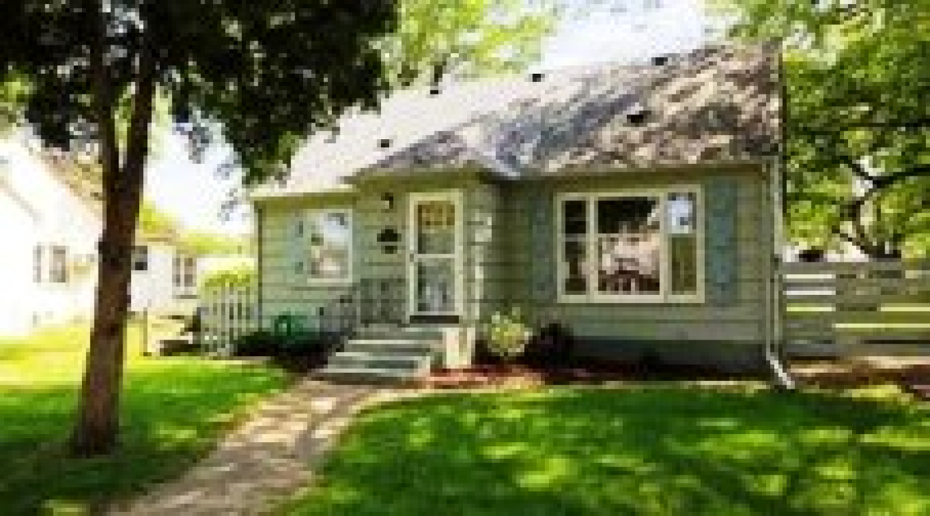 Photo of a small house from the front, with a tree shading the house and expanse of front lawn.