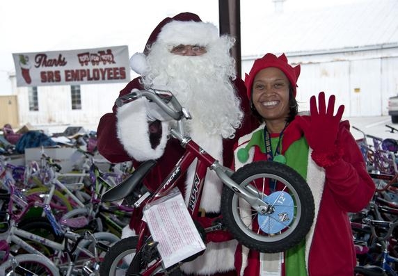 An elf from DOE's Savannah River Site poses with Santa Claus, who holds a bike, one of the more than 14,200 toys federal employees and contractors donated to the U.S. Marine Toys for Tots Program. Mounds of bikes and other donated toys for the program can be seen in the background. An elf from DOE's Savannah River Site poses with Santa Claus, who holds a bike, one of the more than 14,200 toys federal employees and contractors donated to the U.S. Marine Toys for Tots Program. Mounds of bikes and other donated toys for the program can be seen in the background.