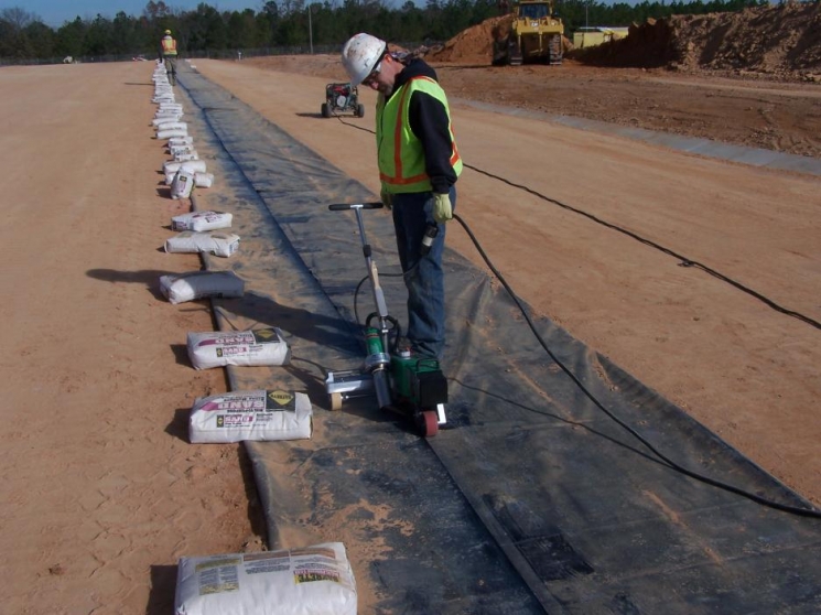 The liner installer heat-welds a sand anchor closed. The sand anchors are installed under the liner and across the length of the slit trench to keep the liner in place and minimize the effects of wind lift. The liner installer heat-welds a sand anchor closed. The sand anchors are installed under the liner and across the length of the slit trench to keep the liner in place and minimize the effects of wind lift.
