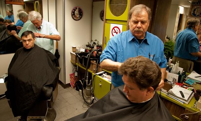 Ron Wilson, left, cuts Joe Conklin's hair while David Besenyei prepares to trim the hair of another customer. | Energy Department Image | Photo by Hantz Leger, Contractor 
