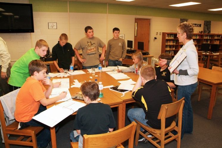 Kelly Layne of the LATA Kentucky team tells Heath Middle School students how to use zinc pennies in an experiment with differing known and unknown solutions. Facing, from left, are students Atherton Milford, McKenzie Moss, Trevor Kendall, Max Kolb, and James Michael Dodd.