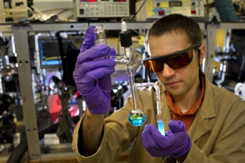 In this photo, Brookhaven scientist Dmitry Polyansky examines a vial containing a specialized catalyst designed to help convert solar energy into fuel. Producing clean-burning hydrogen fuel from just sunlight and water requires custom-built catalysts for water oxidation -- the part of the water-splitting process that generates oxygen atoms. A tiny amount of the solid catalyst, developed in collaboration with the University of Houston, dissolves and turns the water that lovely shade of blue. | Photo courtesy of Brookhaven National Laboratory. In this photo, Brookhaven scientist Dmitry Polyansky examines a vial containing a specialized catalyst designed to help convert solar energy into fuel. Producing clean-burning hydrogen fuel from just sunlight and water requires custom-built catalysts for water oxidation -- the part of the water-splitting process that generates oxygen atoms. A tiny amount of the solid catalyst, developed in collaboration with the University of Houston, dissolves and turns the water that lovely shade of blue. | Photo courtesy of Brookhaven National Laboratory.