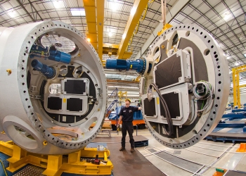 In Jonesboro, Arkansas, a Nordex USA employee stands between utility-scale components that will eventually make up a completed wind turbine. Under the Recovery Act, Nordex USA received a tax credit to assist in the creation of the Jonesboro manufacturing facility, which opened in October 2010. | Photo courtesy of Nordex USA. In Jonesboro, Arkansas, a Nordex USA employee stands between utility-scale components that will eventually make up a completed wind turbine. Under the Recovery Act, Nordex USA received a tax credit to assist in the creation of the Jonesboro manufacturing facility, which opened in October 2010. | Photo courtesy of Nordex USA.