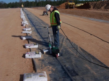The liner installer heat-welds a sand anchor closed. The sand anchors are installed under the liner and across the length of the slit trench to keep the liner in place and minimize the effects of wind lift. The liner installer heat-welds a sand anchor closed. The sand anchors are installed under the liner and across the length of the slit trench to keep the liner in place and minimize the effects of wind lift.