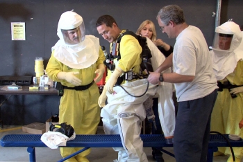 Trainers adjust a Plutonium Finishing Plant employeeâs harness that carries the respirator, cooling system, and other equipment safely inside the protective suit. Trainers adjust a Plutonium Finishing Plant employeeâs harness that carries the respirator, cooling system, and other equipment safely inside the protective suit.