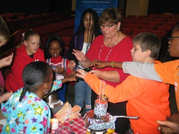 Sixth graders compare emissions from a candleâinvisible until they hold a mirror close to the flame and watch carbon blacken its surface. The same mirror grows steamy but clear when held up to the water vapor piping out of the tea kettle. Sharon Cosgrove, of the Energy Departmentâs Geothermal Technologies Office, talks with the students about energy options: burning hydrocarbons to boil water and generate steam or letting the Earth heat water naturally with geothermal energy. | Photo courtesy of Old Mill Middle School North Sixth graders compare emissions from a candleâinvisible until they hold a mirror close to the flame and watch carbon blacken its surface. The same mirror grows steamy but clear when held up to the water vapor piping out of the tea kettle. Sharon Cosgrove, of the Energy Departmentâs Geothermal Technologies Office, talks with the students about energy options: burning hydrocarbons to boil water and generate steam or letting the Earth heat water naturally with geothermal energy. | Photo courtesy of Old Mill Middle School North