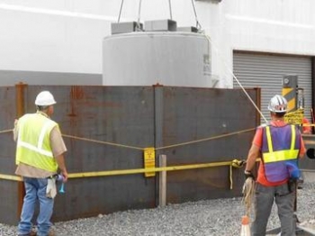 Workers place a solidified sludge liner into shielded storage. A spotter keeps a close eye on all lifts and heavy equipment movements. Workers place a solidified sludge liner into shielded storage. A spotter keeps a close eye on all lifts and heavy equipment movements.