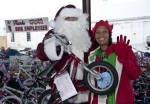 An elf from DOE's Savannah River Site poses with Santa Claus, who holds a bike, one of the more than 14,200 toys federal employees and contractors donated to the U.S. Marine Toys for Tots Program. Mounds of bikes and other donated toys for the program can be seen in the background.