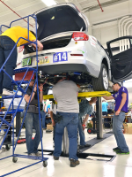 The University of Washington team works on their vehicle while lifted on a hoist. Teams are working in a garage that is fully equipped with tools that will help them make the most of their time this week. | Photo courtesy of EcoCAR 2.